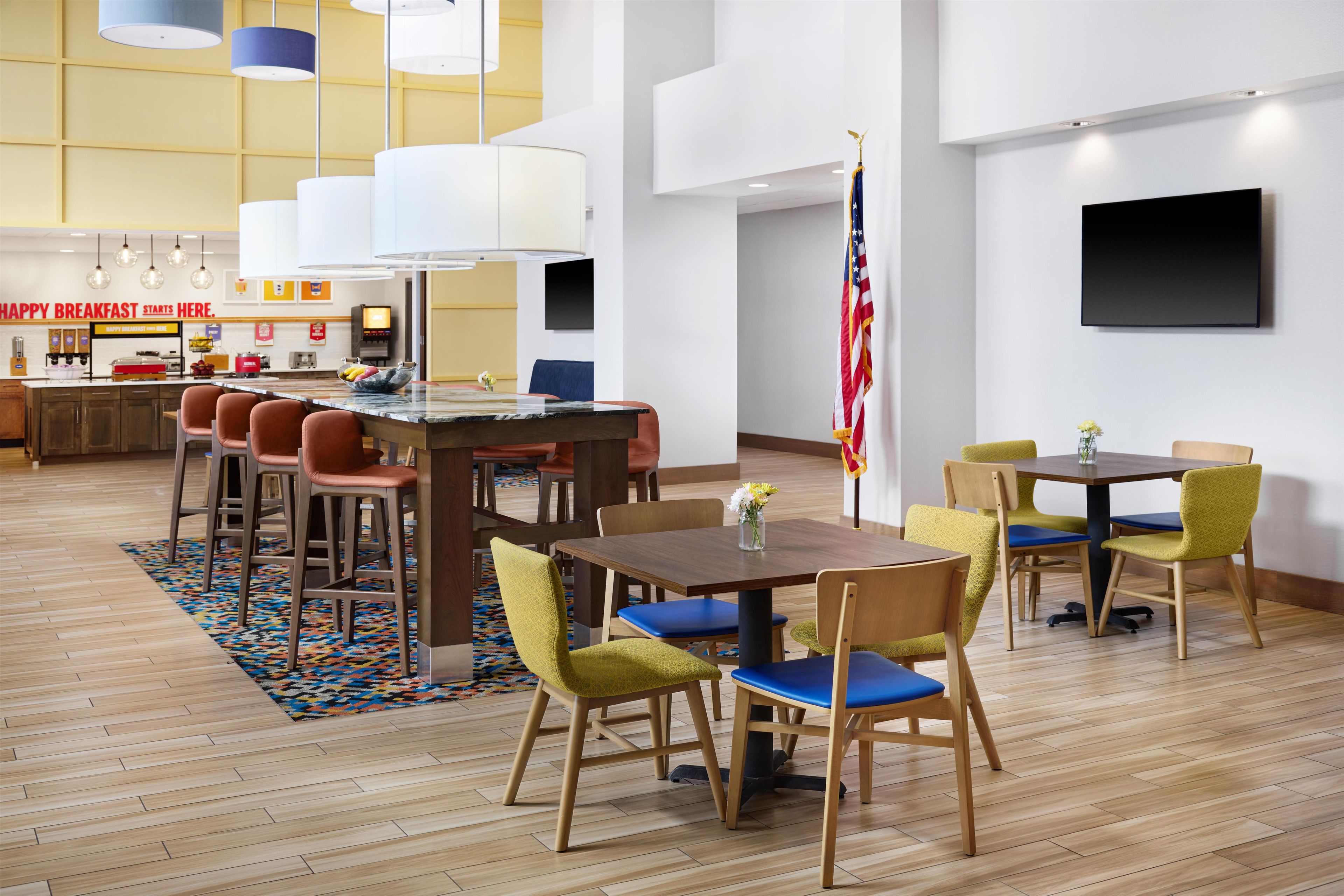 A hotel dining area with a breakfast bar, multiple tables, and chairs.
