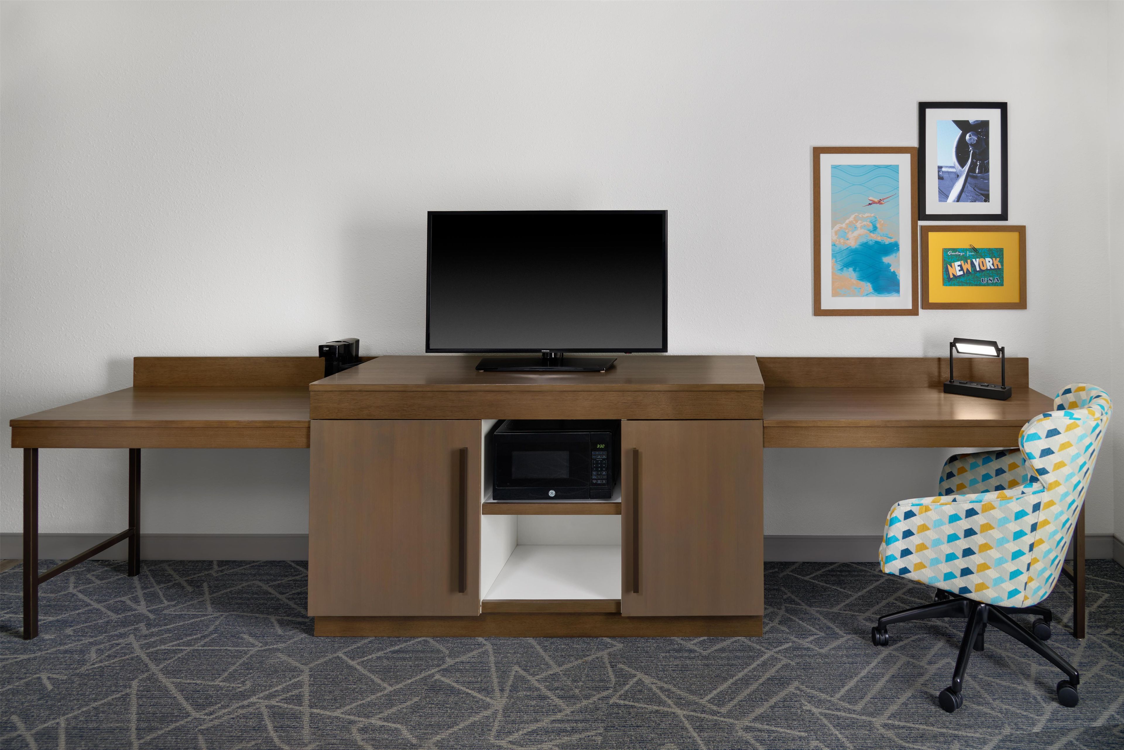 Een modern bureau met een flatscreen monitor, een ingebouwde magnetron en een bureaustoel met een patroon.