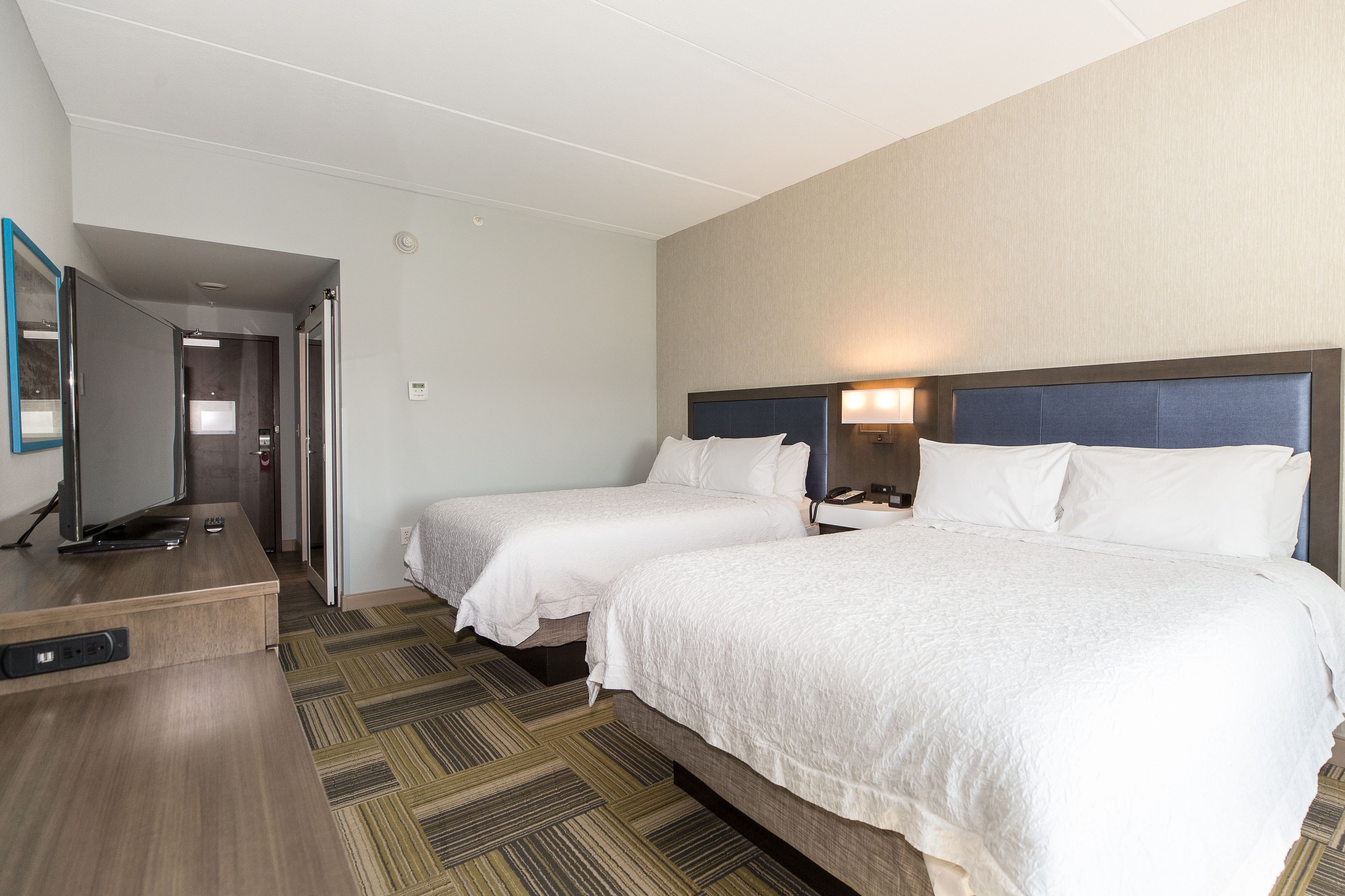 A hotel room with two beds, a desk with a television, and a carpeted floor.