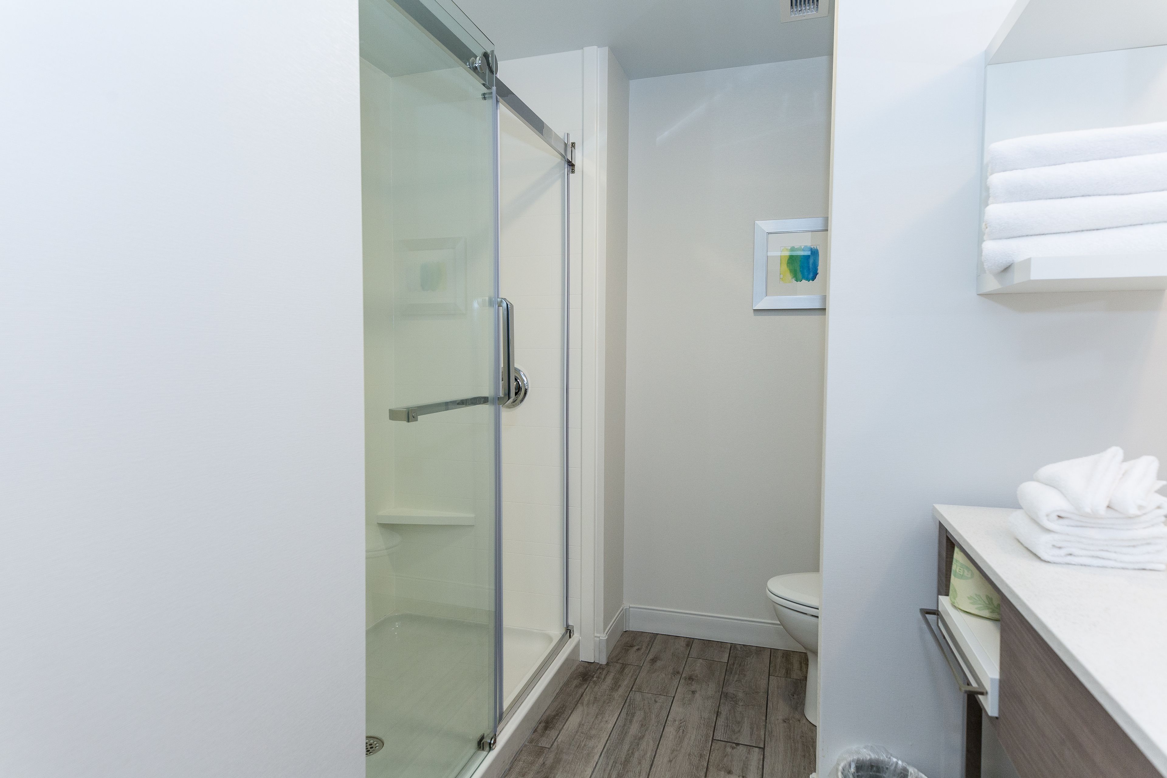A modern bathroom with a glass shower enclosure, a toilet, and a sink area with neatly folded towels.