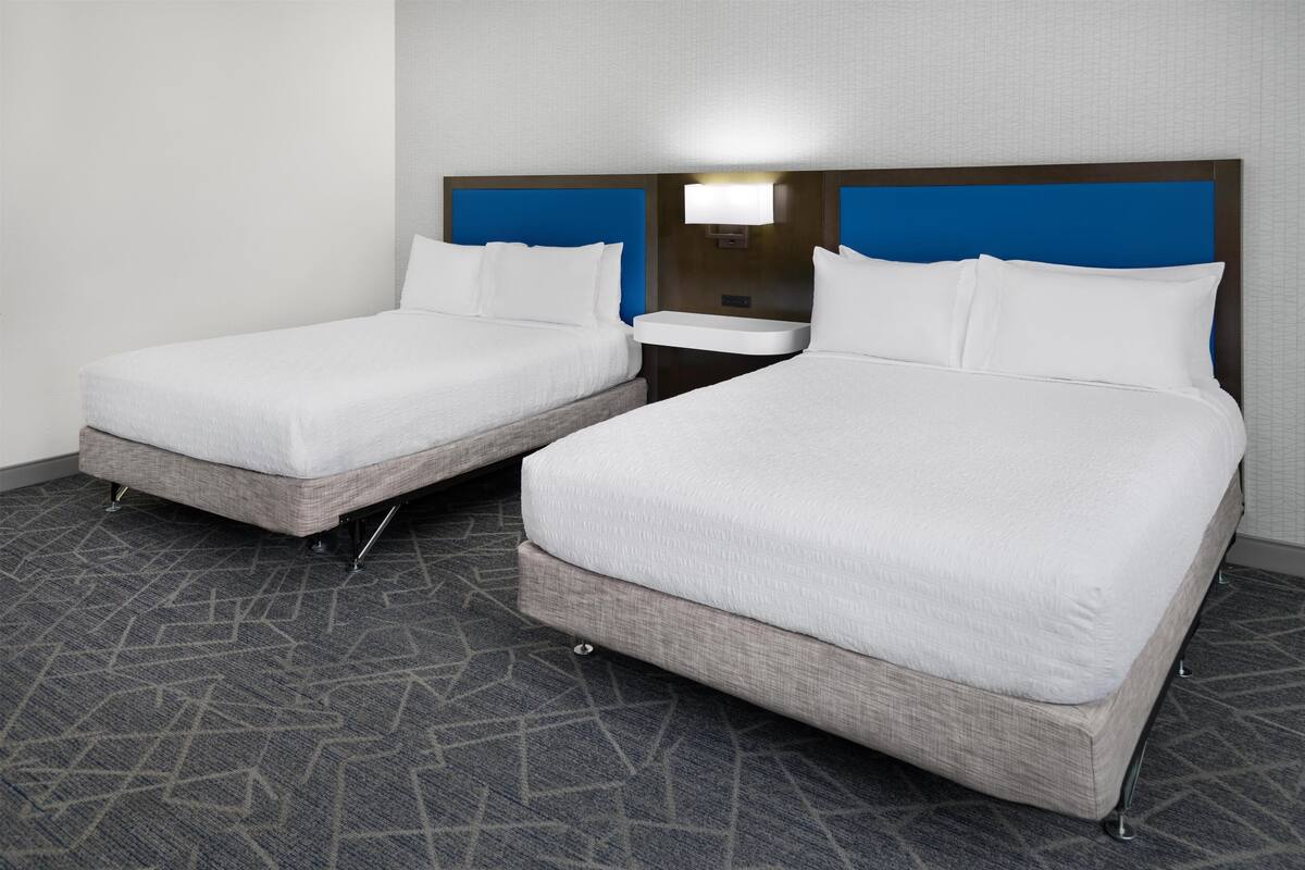 A hotel room with two beds, a nightstand, and a wall-mounted light.