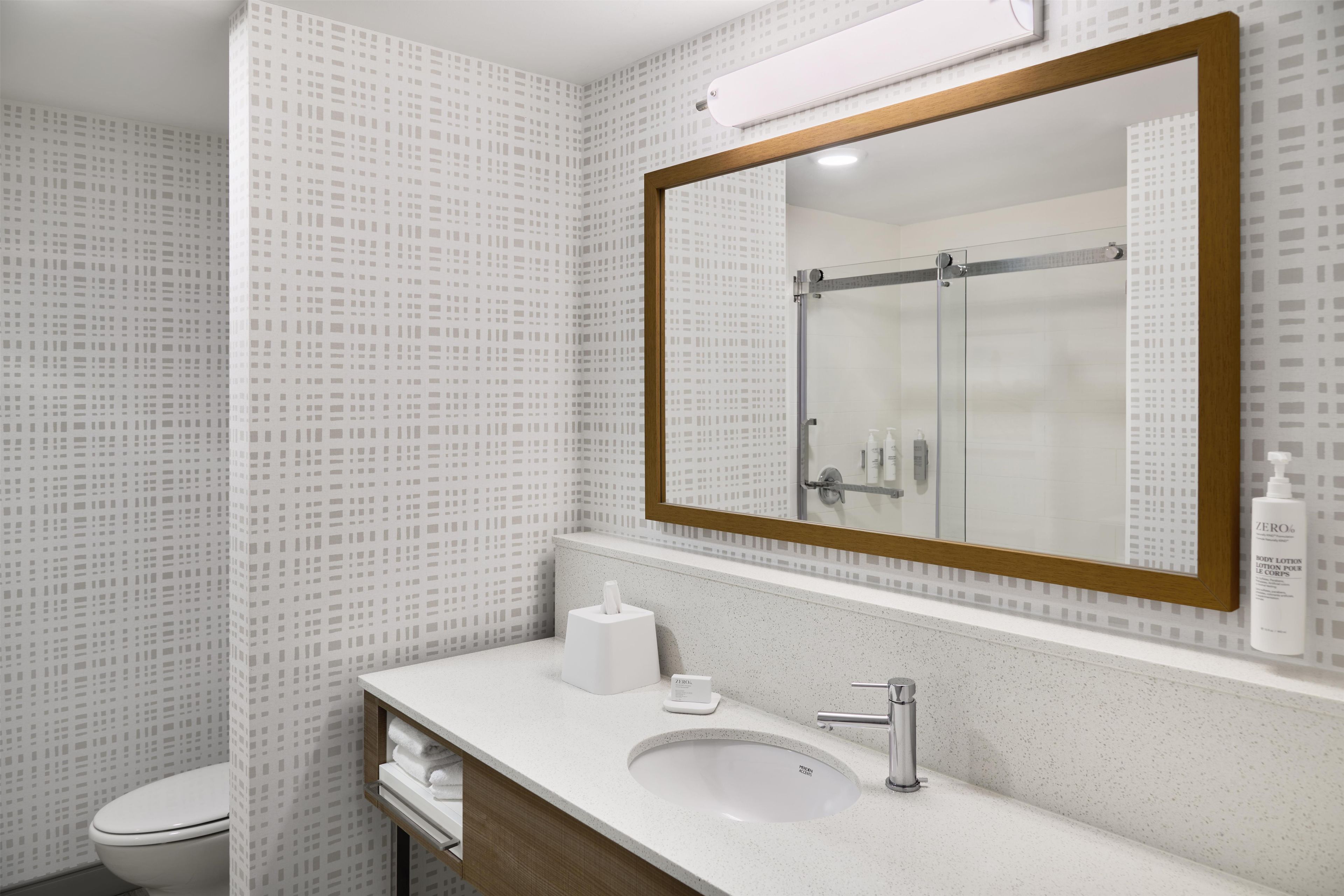 A bathroom with a white sink, a mirror with a wooden frame, a toilet, and a shower area.