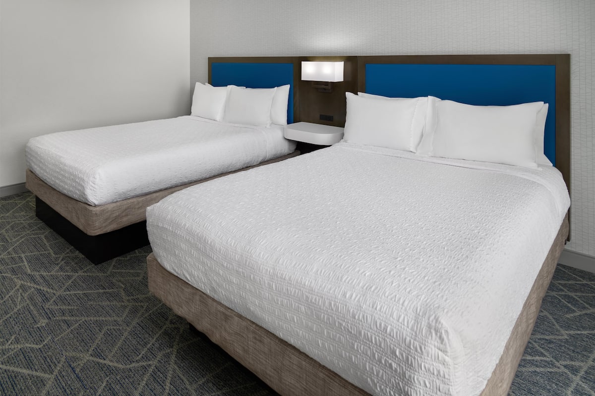 A hotel room with two beds, a nightstand, and a wall-mounted lamp.