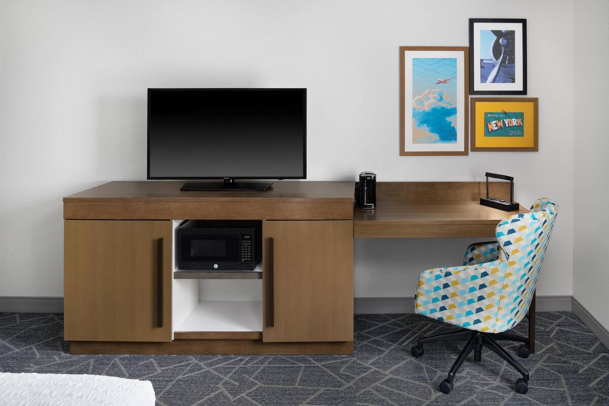 A modern office desk with a flat-screen TV, a coffee maker, and a patterned office chair.