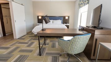 Una habitación de hotel con cama, escritorio, silla, televisor y ventana con cortinas.