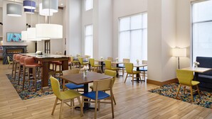 A spacious dining area with multiple tables and chairs, a fireplace, and large windows. - Hampton Inn & Suites Syracuse North Airport Area (Liverpool)