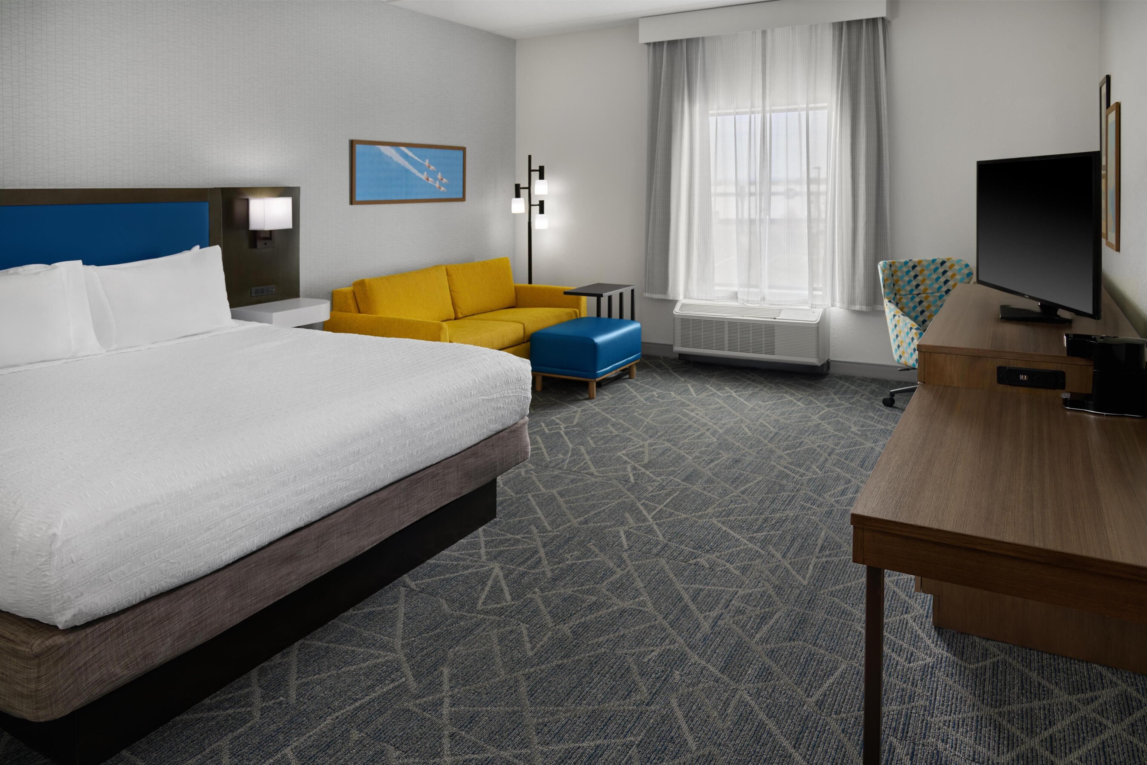 A hotel room with a large bed, a desk, a television, a sofa, and a window with curtains.