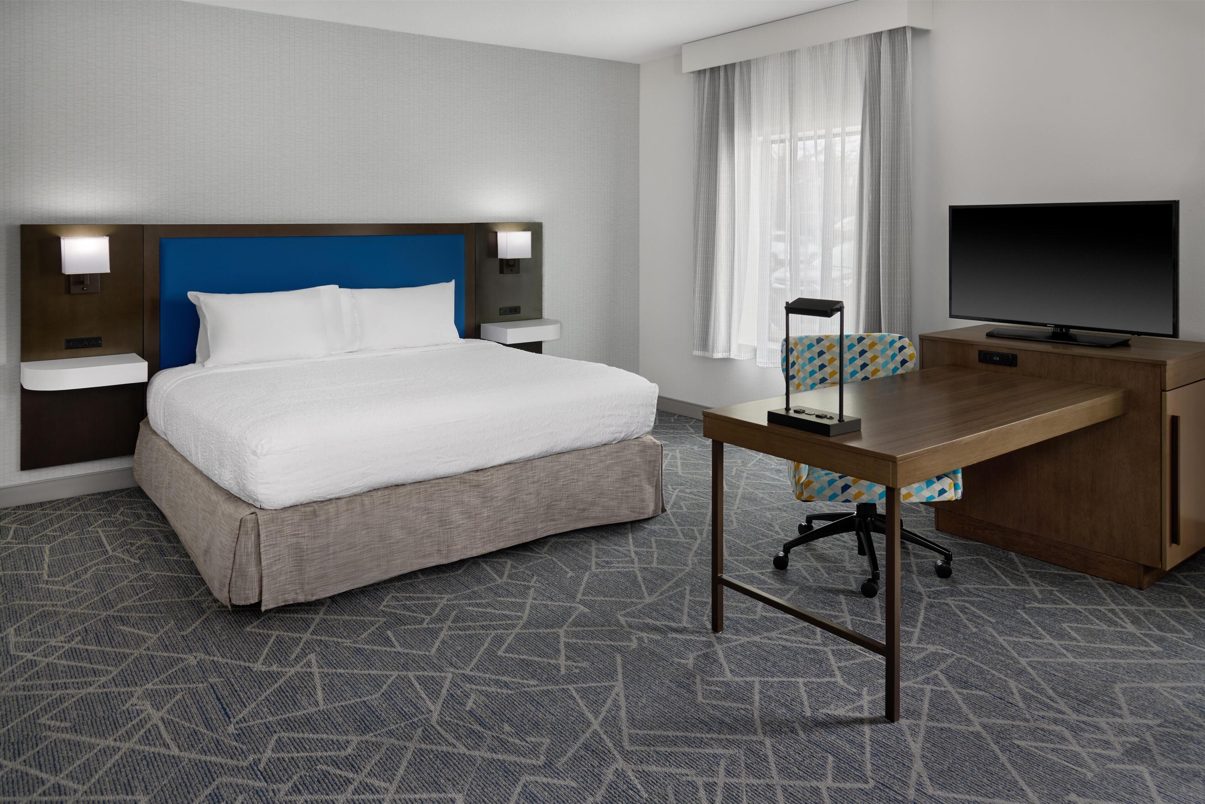 A hotel room with a bed, a desk, a television, and a window with curtains.