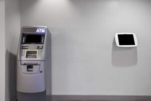 Un cajero automático en una habitación con una pared lisa y un pequeño objeto cuadrado blanco en la pared.