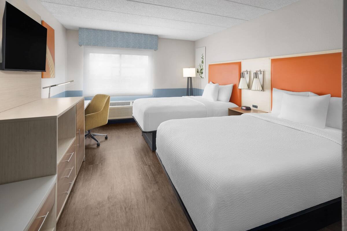 Une chambre d’hôtel avec deux lits, un bureau, une chaise, une télévision et une fenêtre.