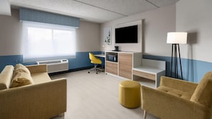 A modern hotel room with a sofa, yellow armchair, and a desk with a computer.