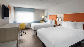 A hotel room with two beds, a desk, a chair, and a TV.