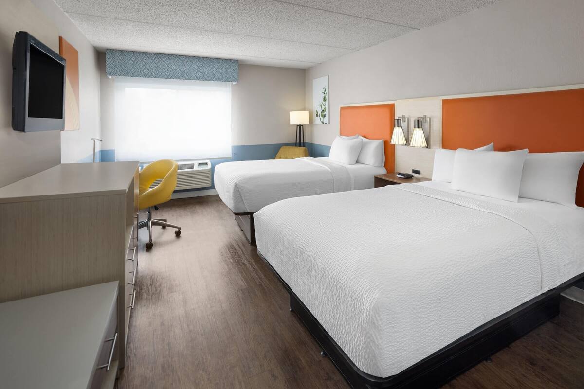 Une chambre d’hôtel avec deux lits, un bureau, une chaise et un téléviseur.