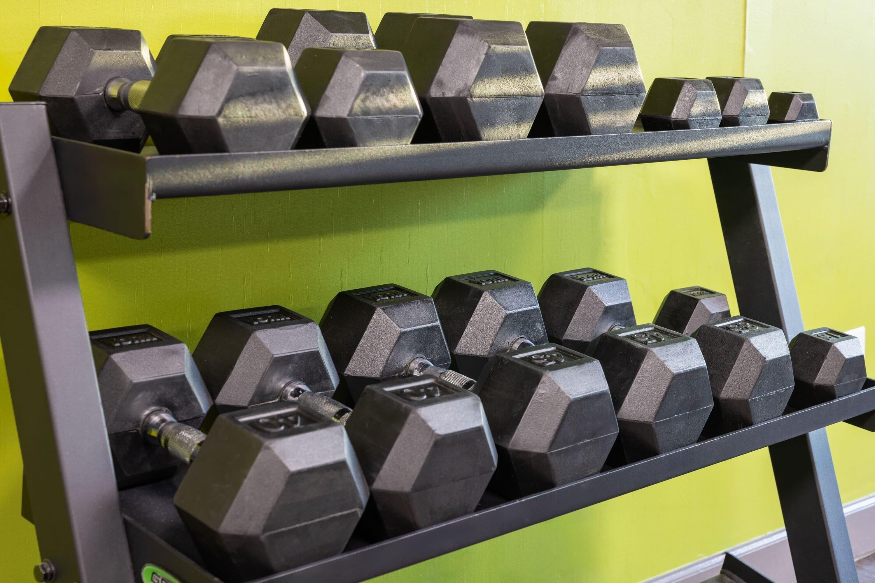 A rack of hexagonal dumbbells in a gym with green walls.