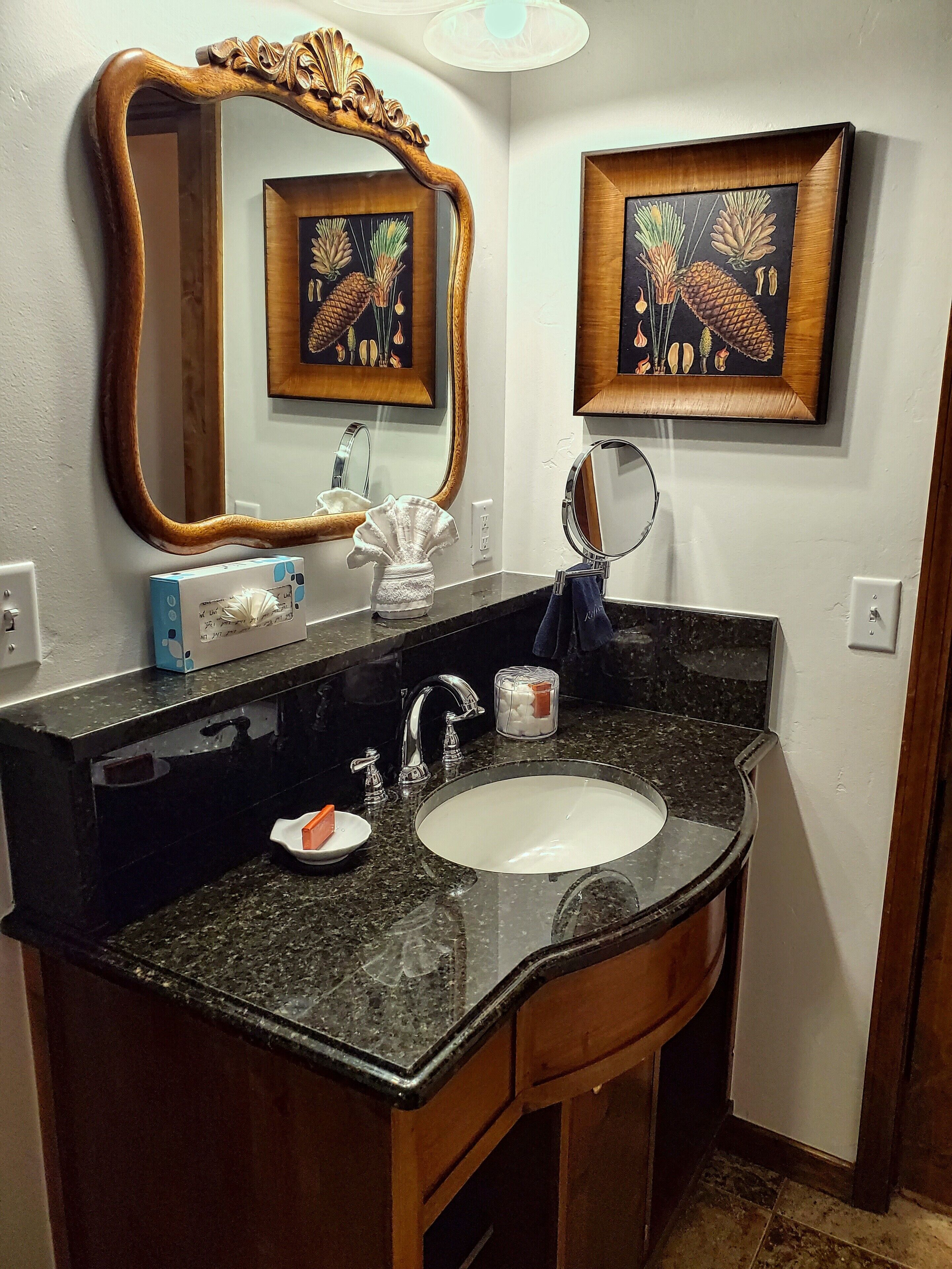 A bathroom with a wooden vanity, a sink, a mirror, and two framed pictures on the wall.