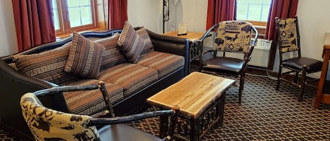 Een woonkamer met een bank, twee gestreept fauteuils, een houten salontafel en een getextureerd vloerkleed.