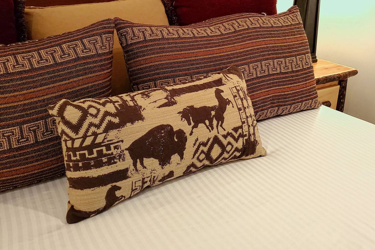 A bed with patterned pillows and a headboard, a nightstand with a lamp, and a wall with a textured pattern.