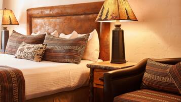 A neatly made bed with patterned pillows, a wooden nightstand with a lamp, and a leather armchair.