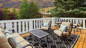 A deck with outdoor furniture, a table, and a view of a hilly landscape.
