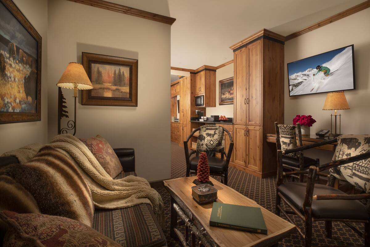 A cozy living room with a fireplace, a dining area with wooden chairs, and a kitchen in the background.