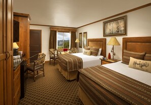 A hotel room with two beds, a desk, a chair, and a window with a mountain view.