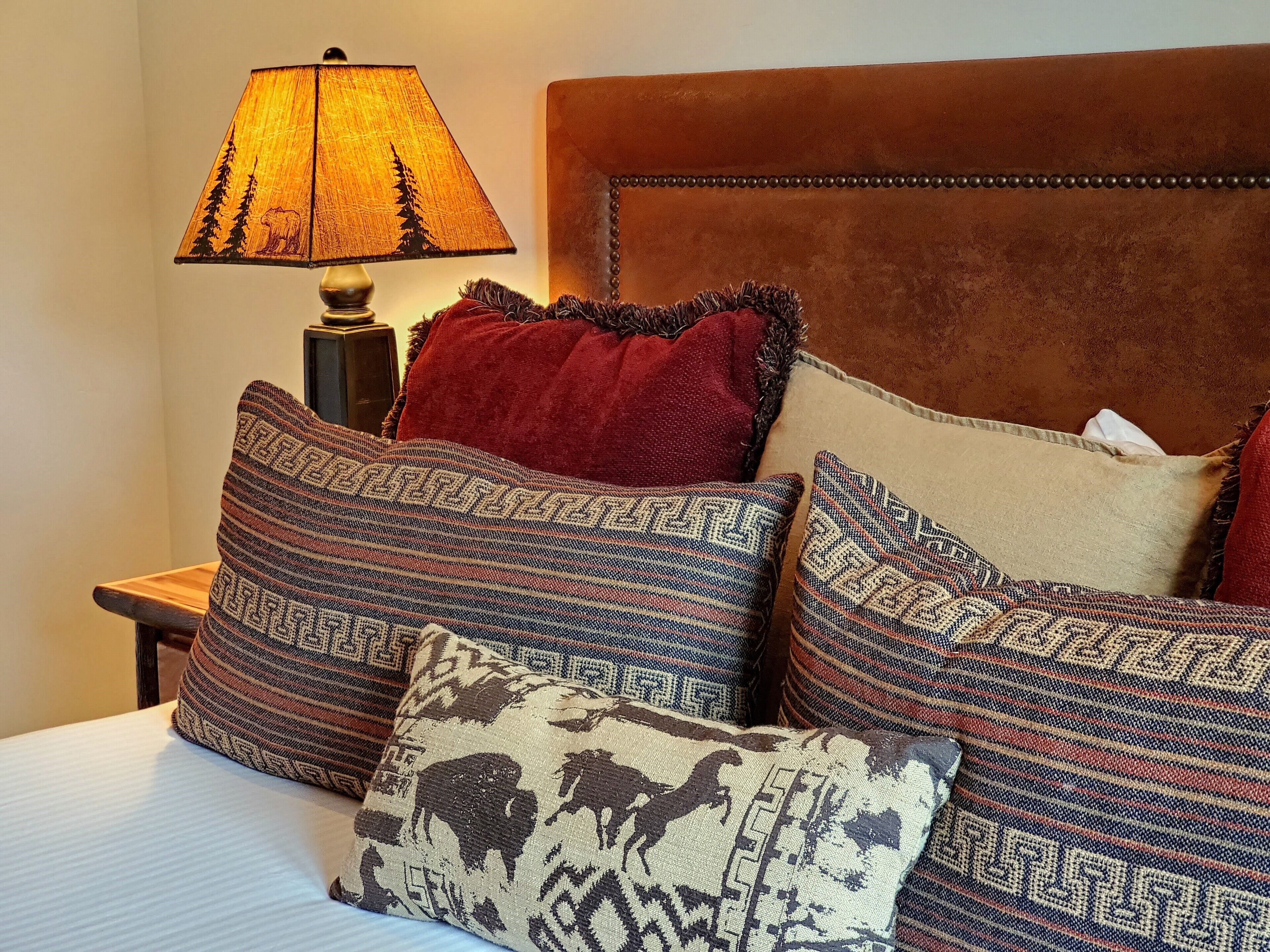 A bed with patterned pillows, a wooden nightstand, and a lamp with a forest design.