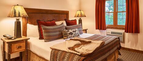 A neatly made bed with patterned bedding, two bedside lamps, a bedside telephone, and a window with curtains.