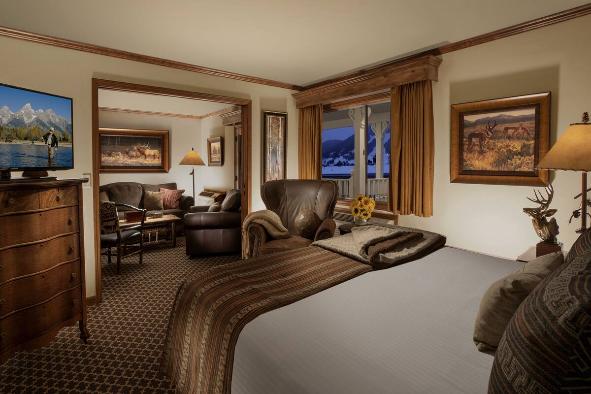 A hotel room with a large bed, a desk, a chair, a television, and a window with a mountain view.