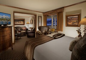 Quarto de hotel com uma cama grande, uma mesa, uma cadeira, televisão e uma janela com vista para as montanhas.