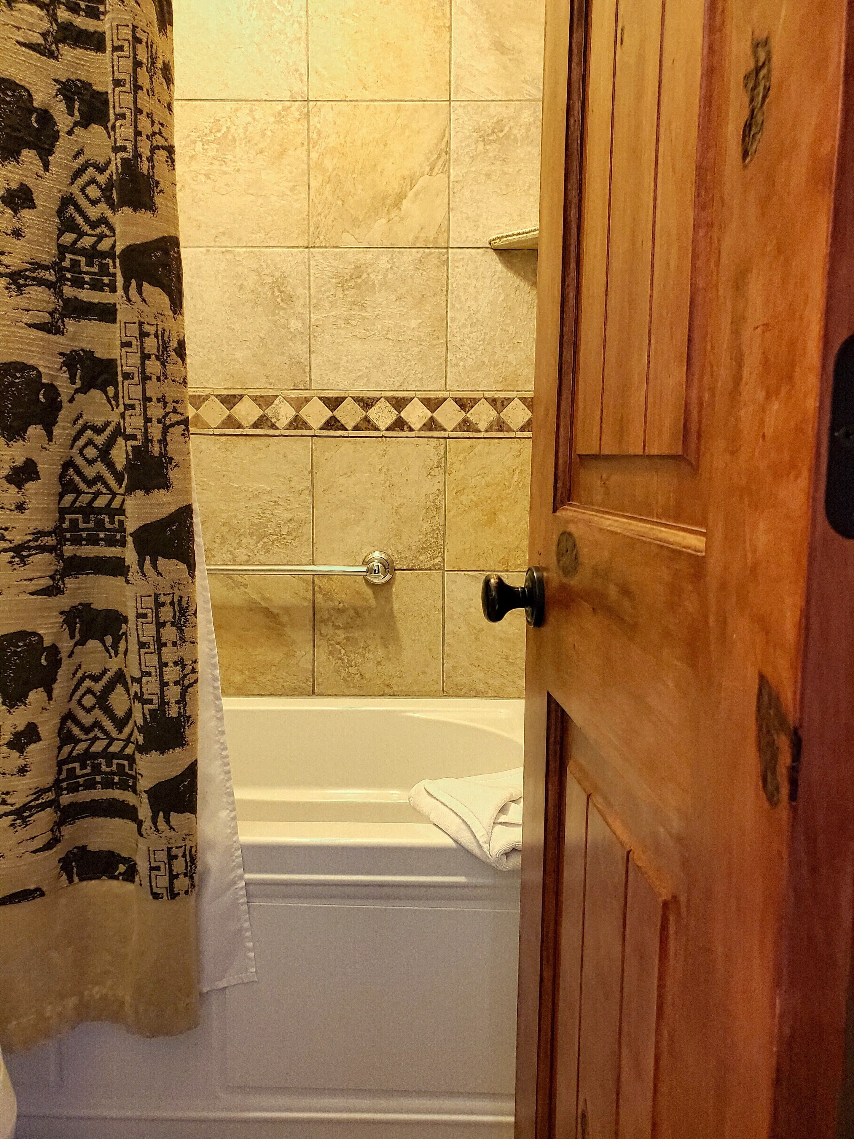 A bathroom with a bathtub, a towel hanging on the wall, and a patterned curtain.