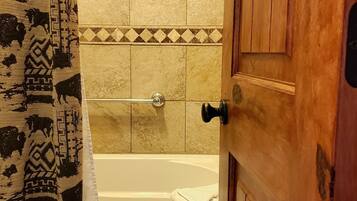A bathroom with a bathtub, a towel hanging on the wall, and a patterned curtain.