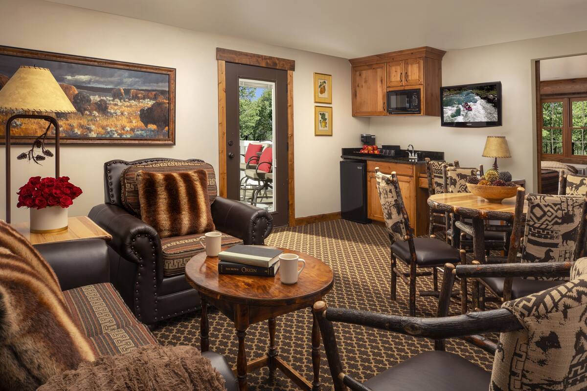 A living room with a fireplace, leather armchairs, a coffee table, and a dining area with patterned chairs.