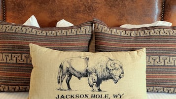 A bed with a patterned pillow featuring a bison illustration and text, set against a brown leather headboard.