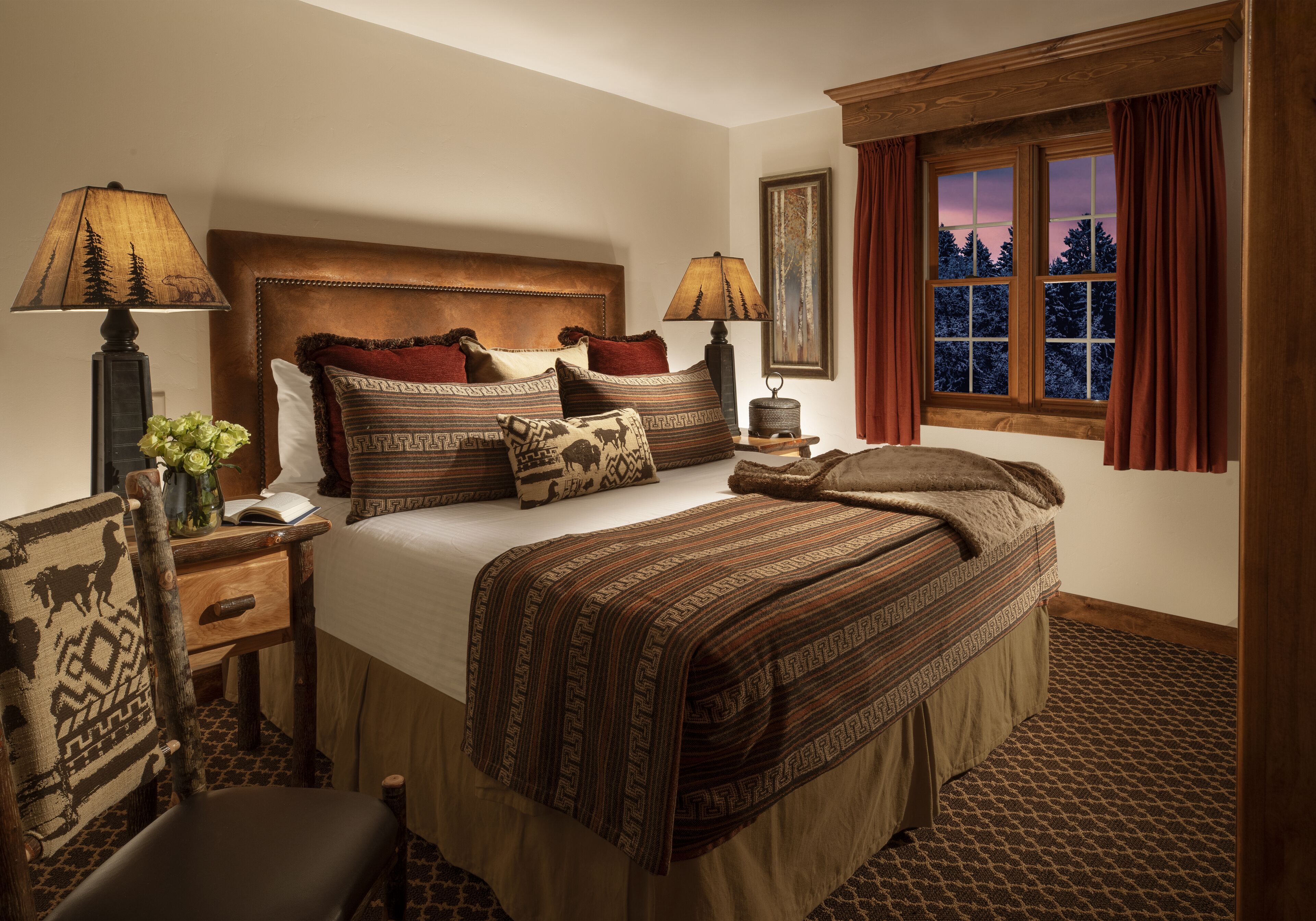 A bedroom with a large bed, two bedside tables, a nightstand, a chair, and a window with curtains.