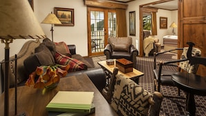 A cozy living room with a sofa, armchairs, a coffee table, and a lamp. There is a door leading to another room and a window with curtains.