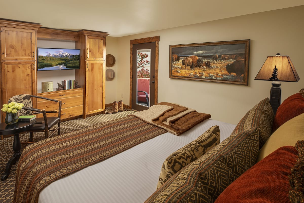 A room with a bed, a desk with a chair, a television, a painting, and a lamp.