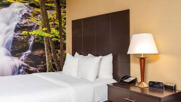 Habitación de hotel con cama, mesita de noche, lámpara y un mural de cascada en la pared.