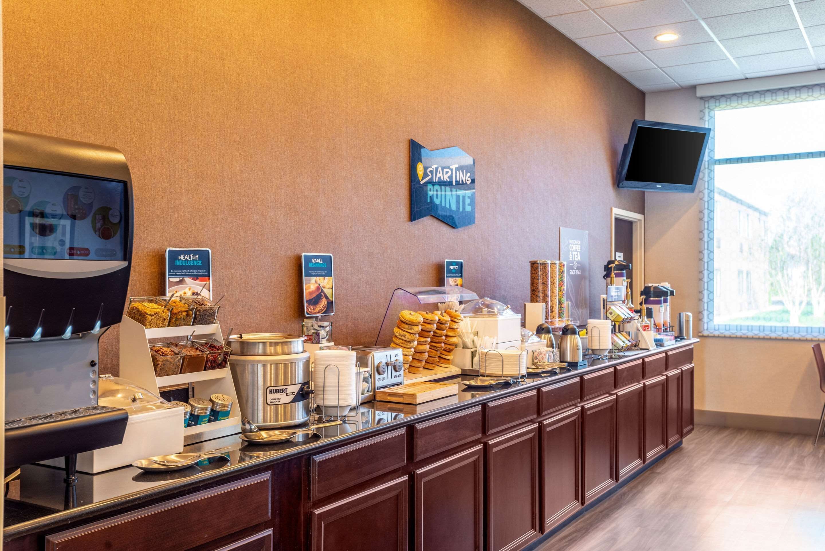 Un mostrador de buffet con diferentes opciones de comida, una estación de café y un televisor montado en la pared.