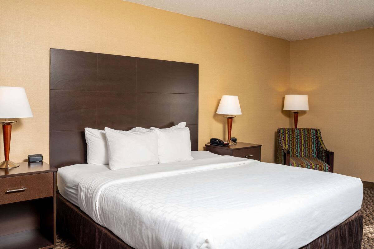 A hotel room with a large bed, two bedside tables, a chair, and a headboard.