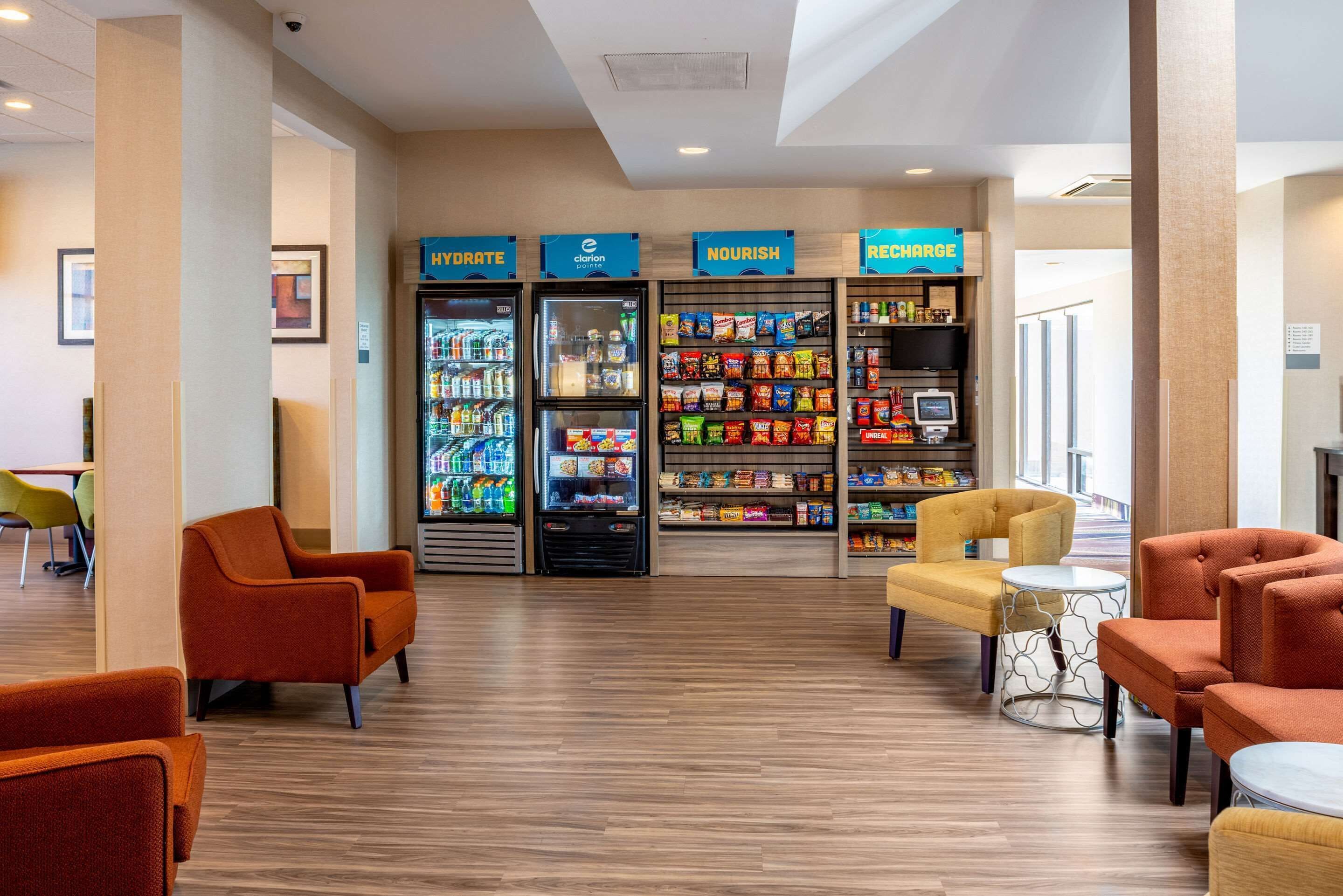 A hotel lobby with seating areas, hydration and nourishment vending machines, and a self-service kiosk.