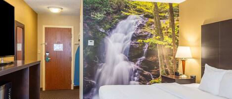Habitación de hotel con cama, televisor, escritorio y una pared con un mural de cascada.