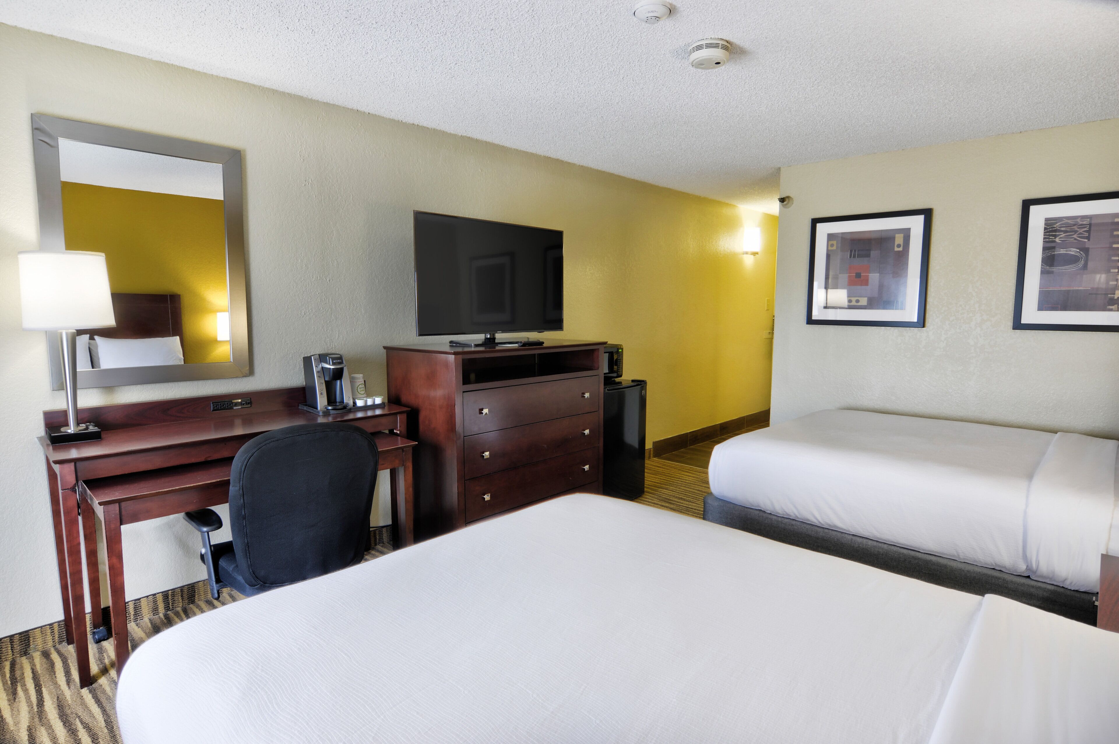 A hotel room with a bed, a desk with a computer, a chair, a television, and a coffee maker.