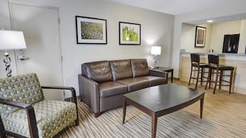 Une chambre d’hôtel équipée d’un canapé, d’un fauteuil, d’une table basse et d’un petit coin repas avec une table et des chaises.