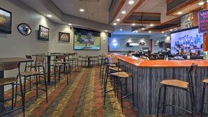 A bar area with a counter, stools, and a screen displaying a sports event. - Holiday Inn St Petersburg N - Clearwater by IHG (Clearwater)