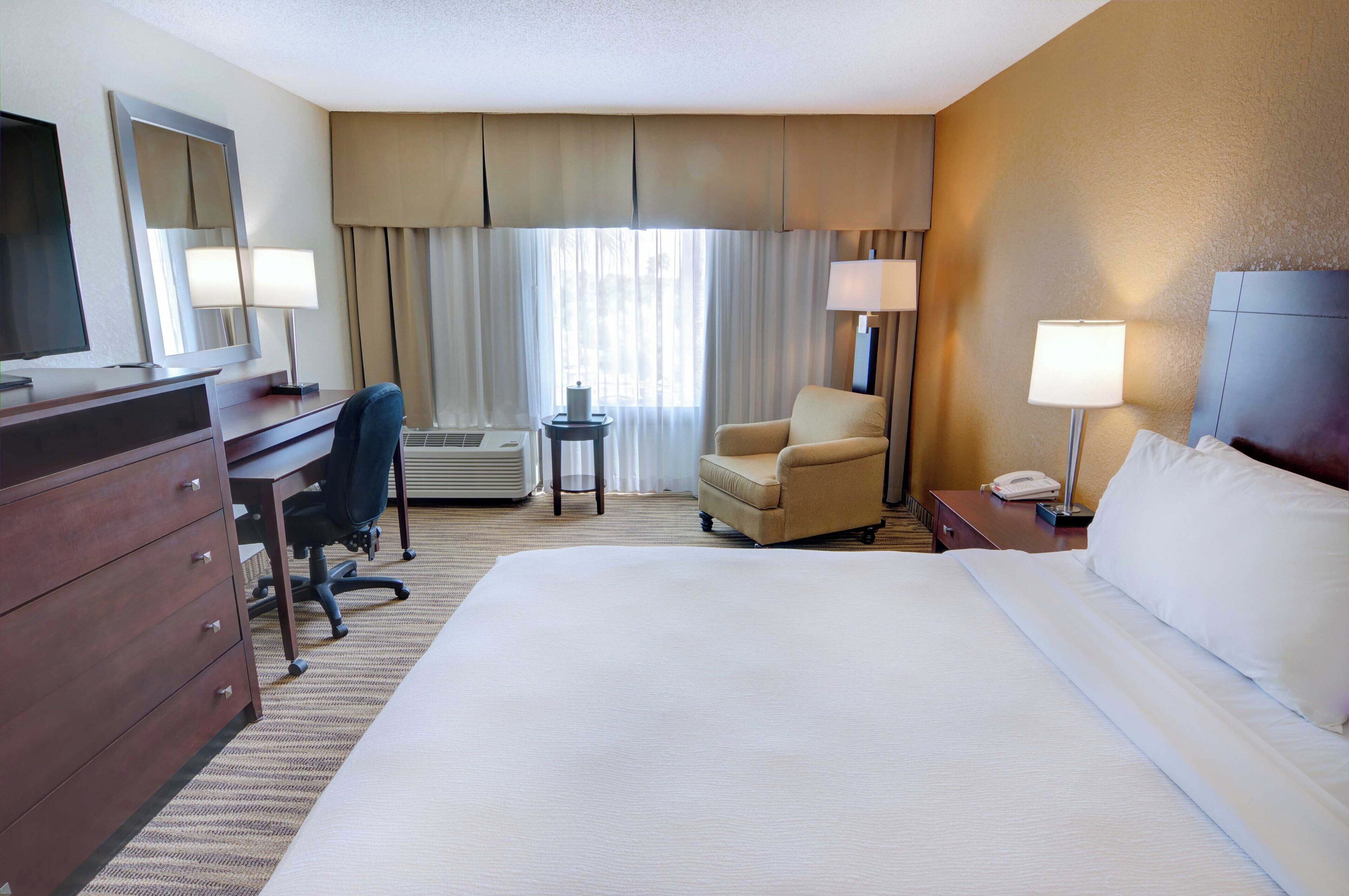 A hotel room with a large bed, a desk with a chair, a television, and a telephone.