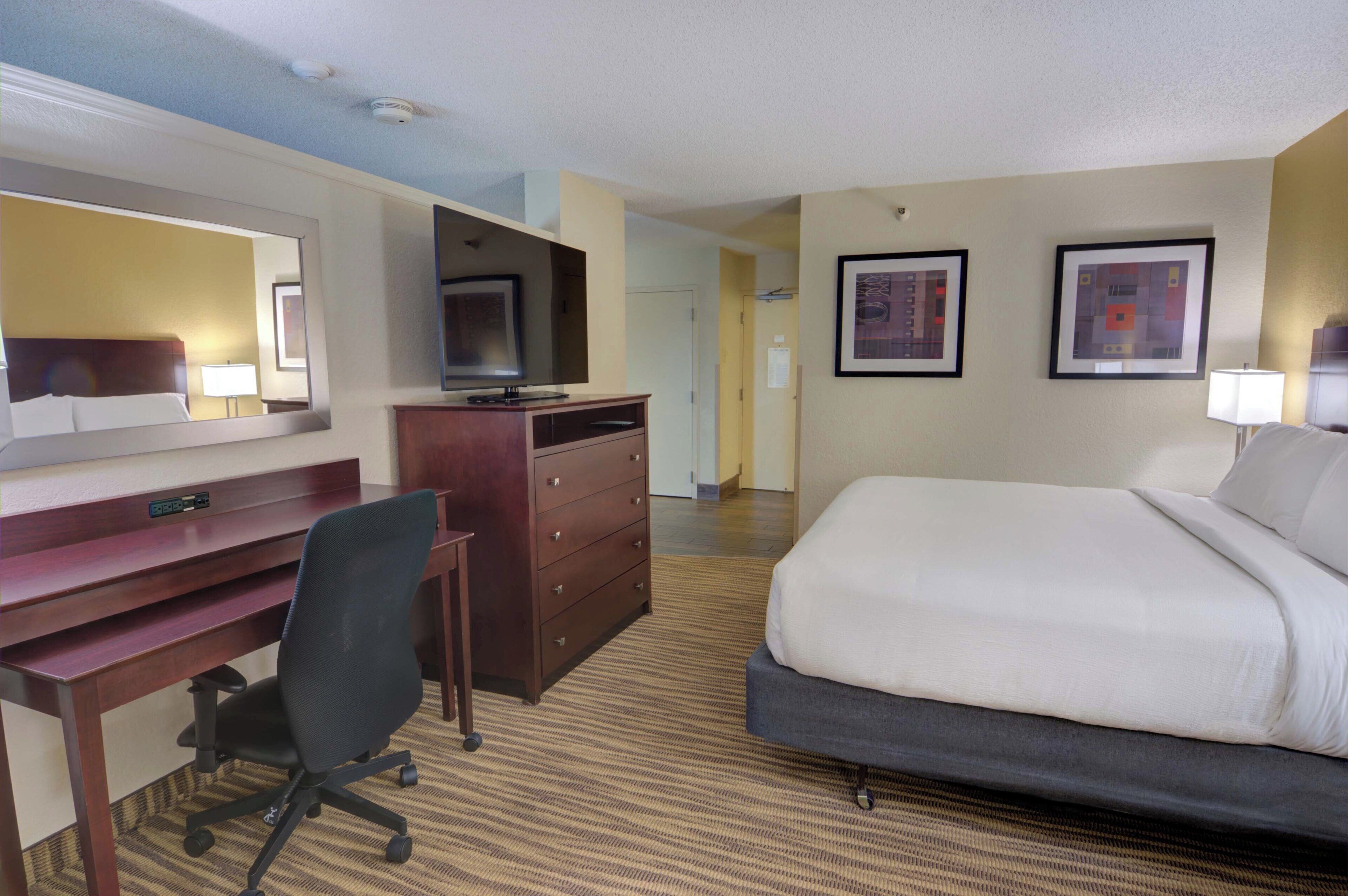 A hotel room with a bed, a desk, a chair, a television, and two framed pictures on the wall.
