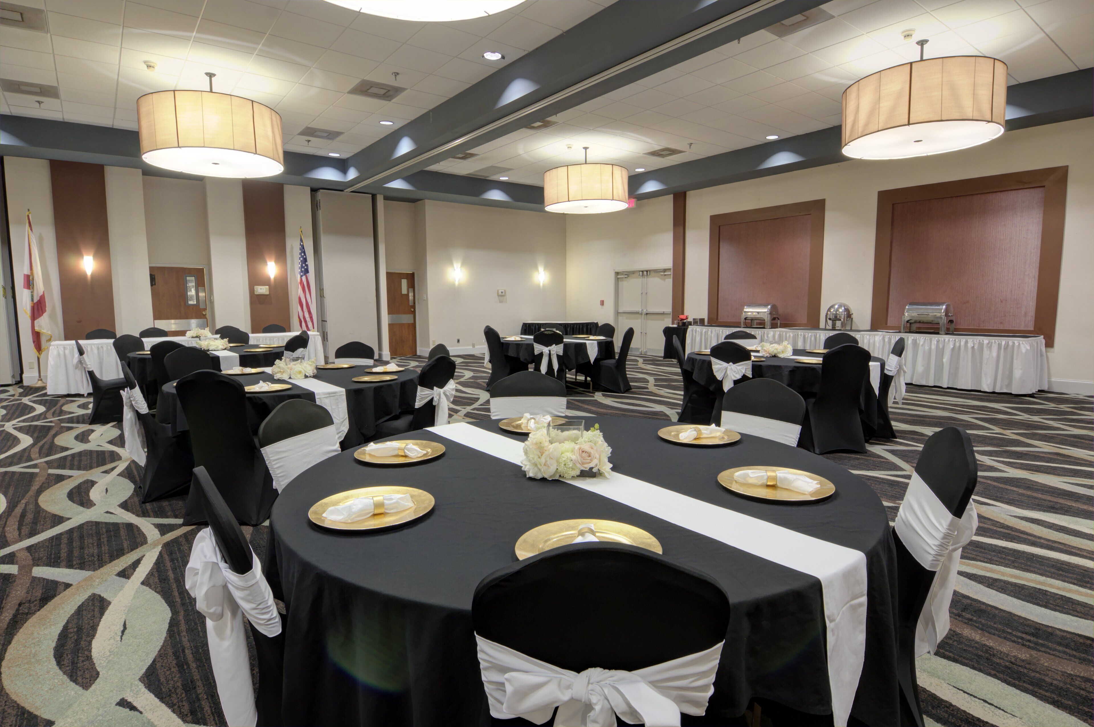 A conference room with round tables, black chairs, and white tablecloths.