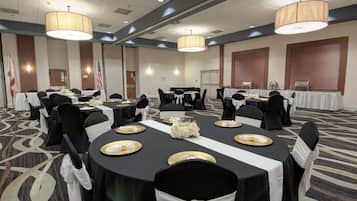 A conference room with round tables, black chairs, and white tablecloths.