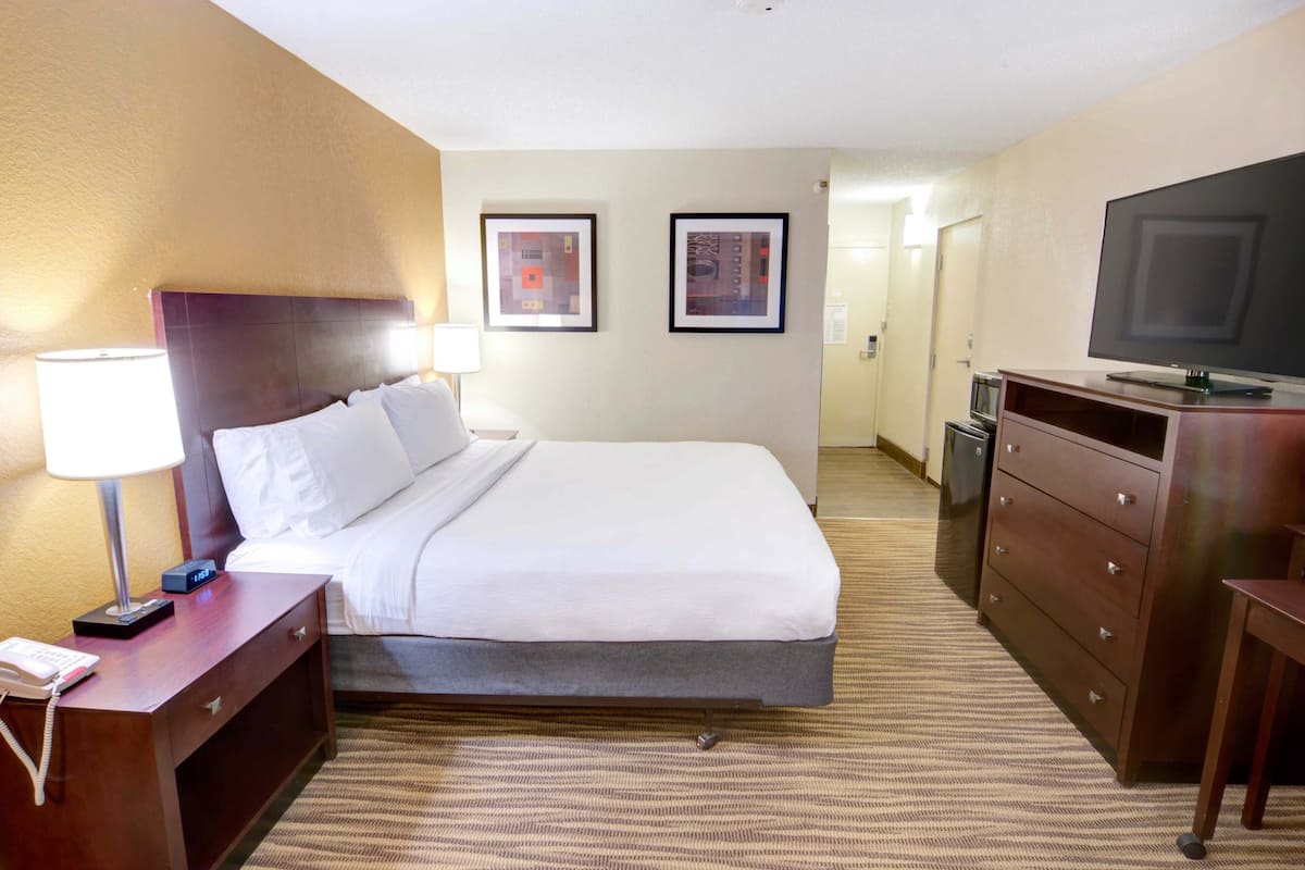 Een hotelkamer met een bed, een bureau met lamp, een kapstok en een televisie.