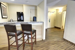 A hotel kitchen with two bar stools, a refrigerator, and a microwave.